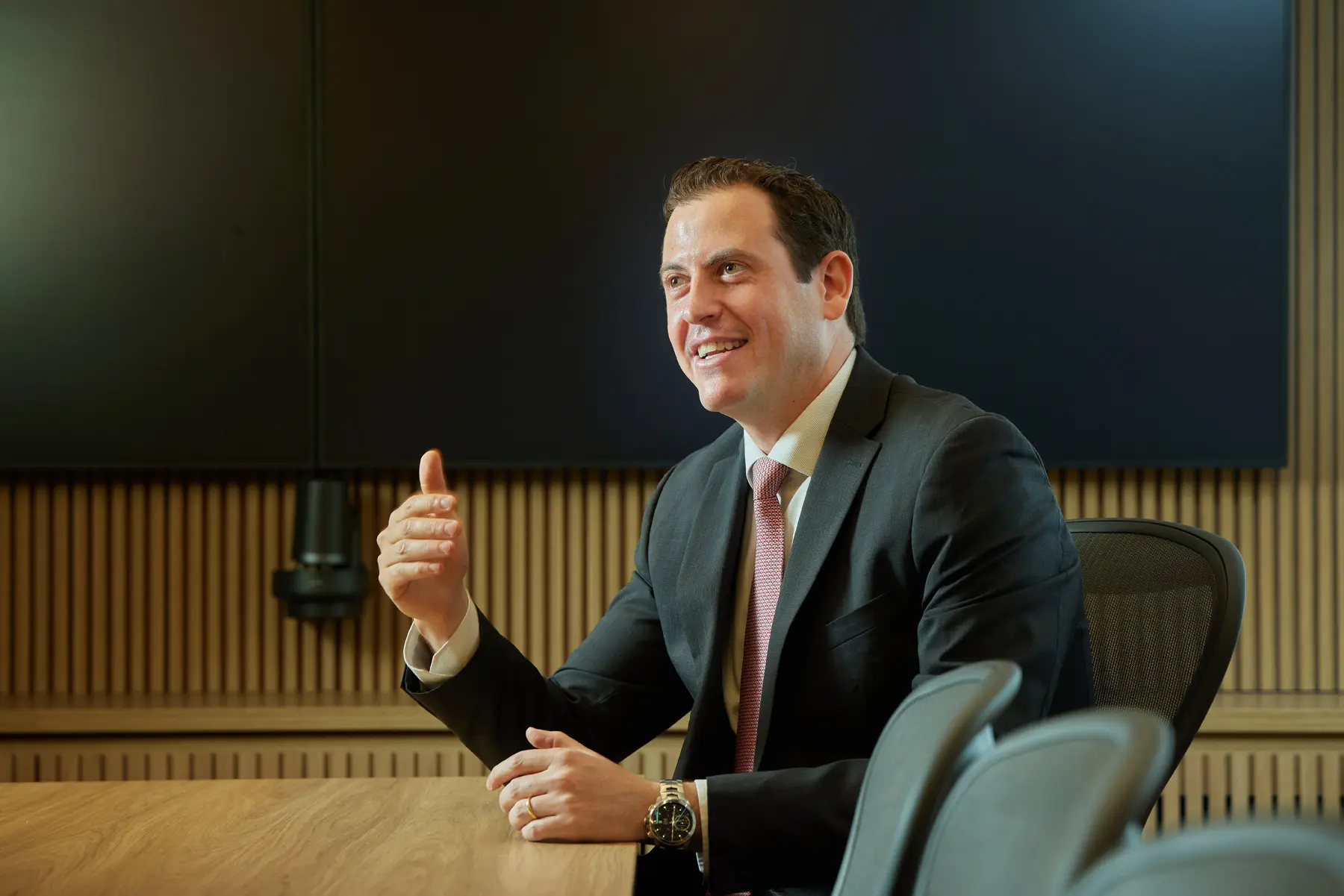 Daniel Rachman, CFO, em reunião corporativa, gesticulando com expressão confiante em ambiente executivo moderno