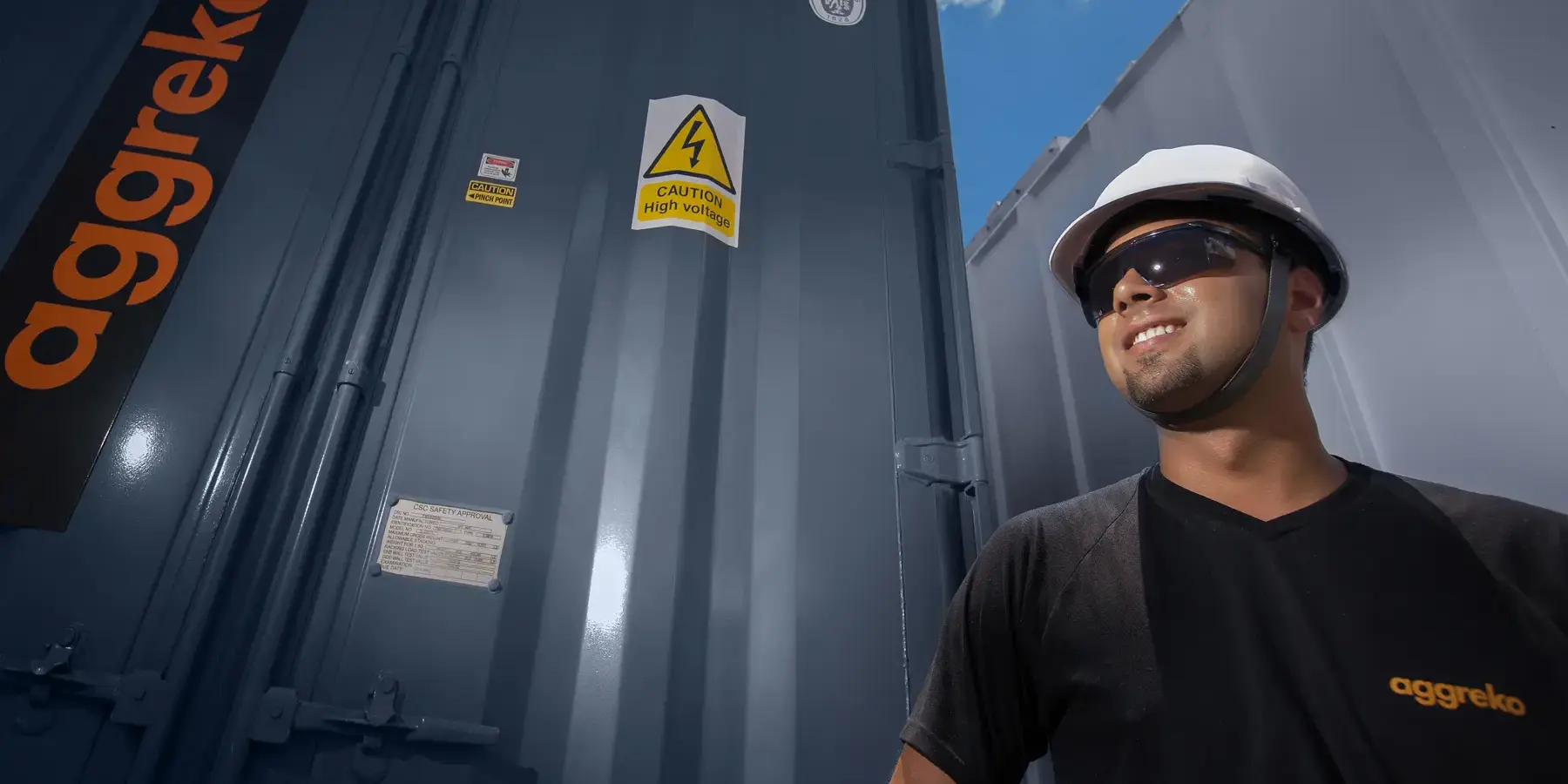Colaborador da Aggreko com capacete e óculos de segurança em frente a unidade de alta tensão