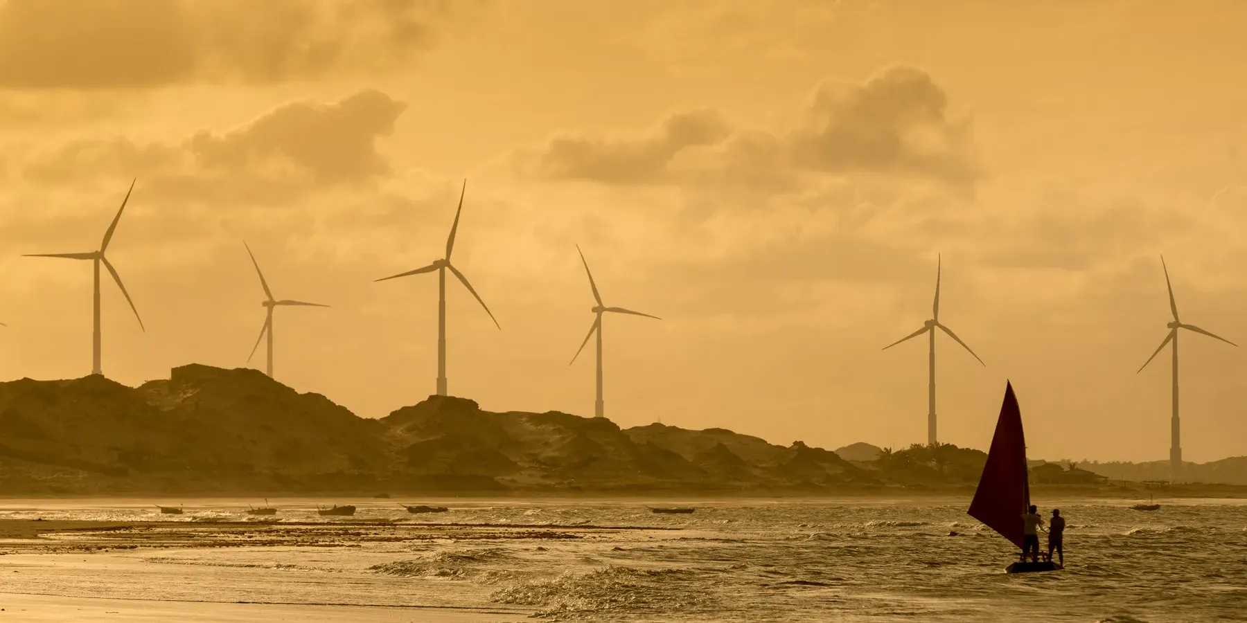 Parque eólico em Icaraí de Amontada, Ceará, com turbinas ao fundo e barco à vela no litoral