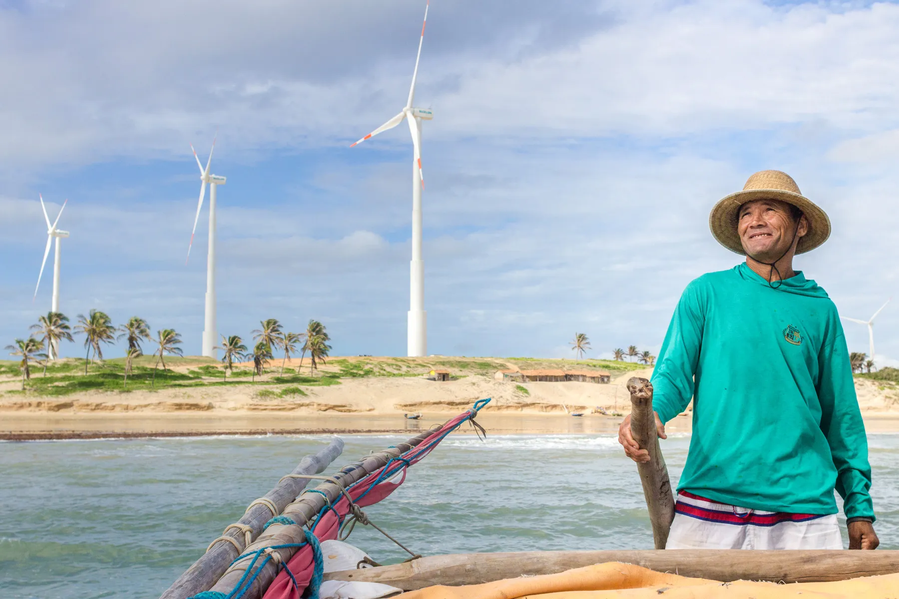 Pescador em Icaraí de Amontada, Ceará, com turbinas eólicas ao fundo e barco de pesca tradicional