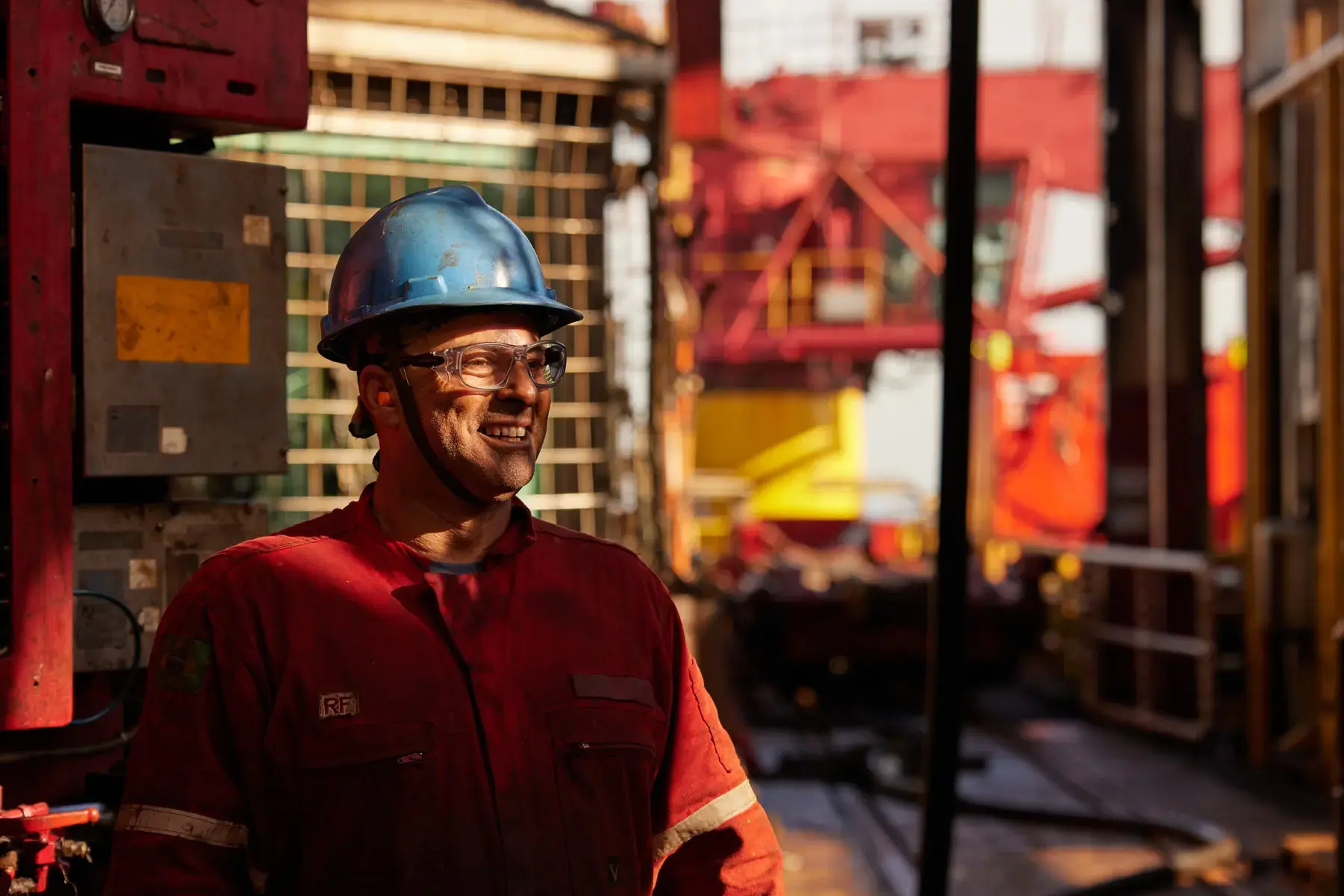 Trabalhador offshore com EPIs no drill floor de navio sonda, com cabine do sondador ao fundo