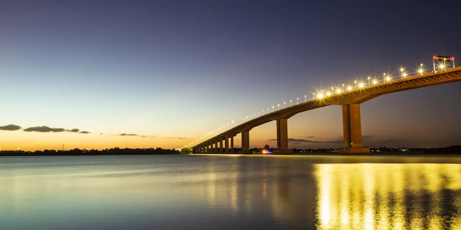 Ponte do Guaíba iluminada ao entardecer em Porto Alegre, RS, com reflexo das luzes sobre o rio