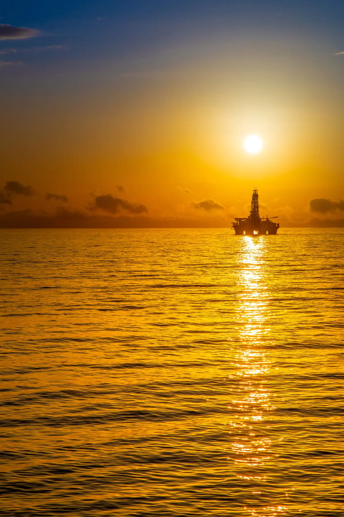 Plataforma semissubmersível offshore silhouetada ao pôr do sol sobre o oceano