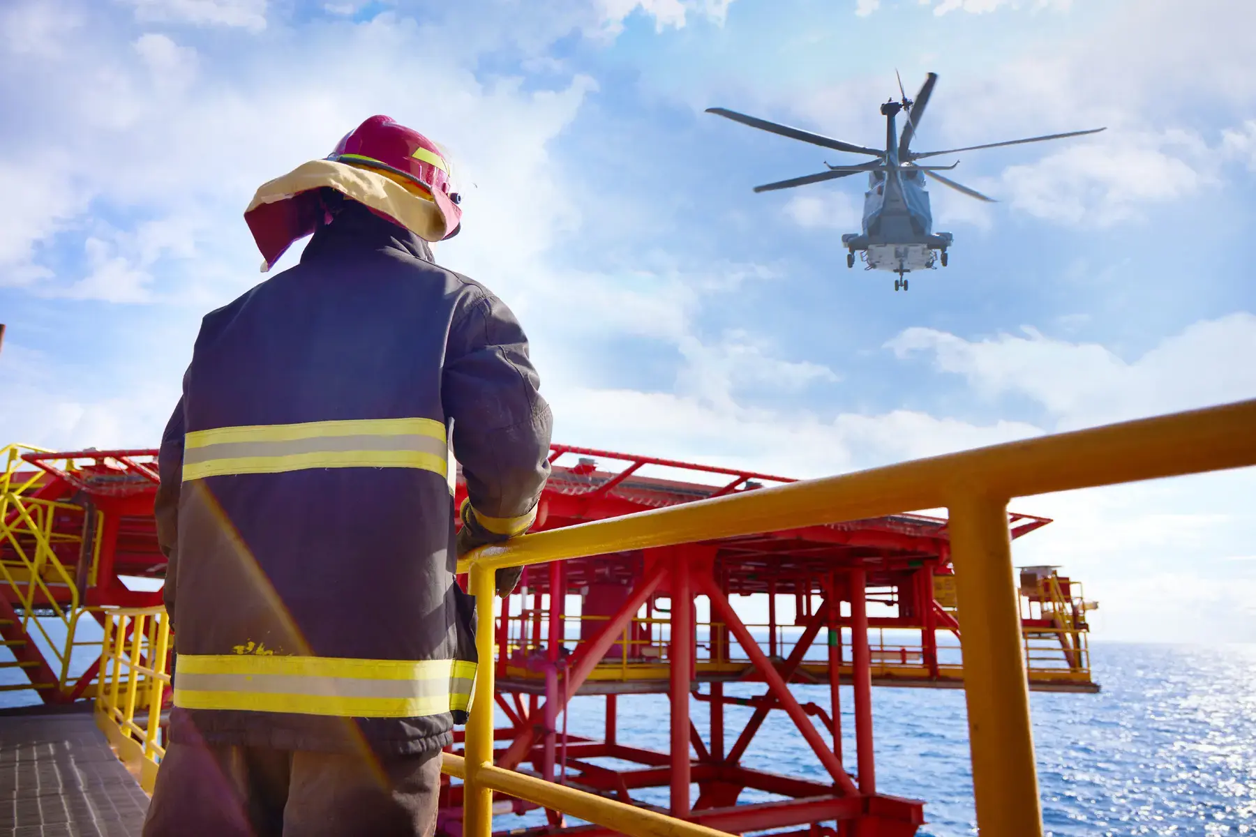 Brigadista em plataforma offshore observa helicóptero em operação sobre o oceano