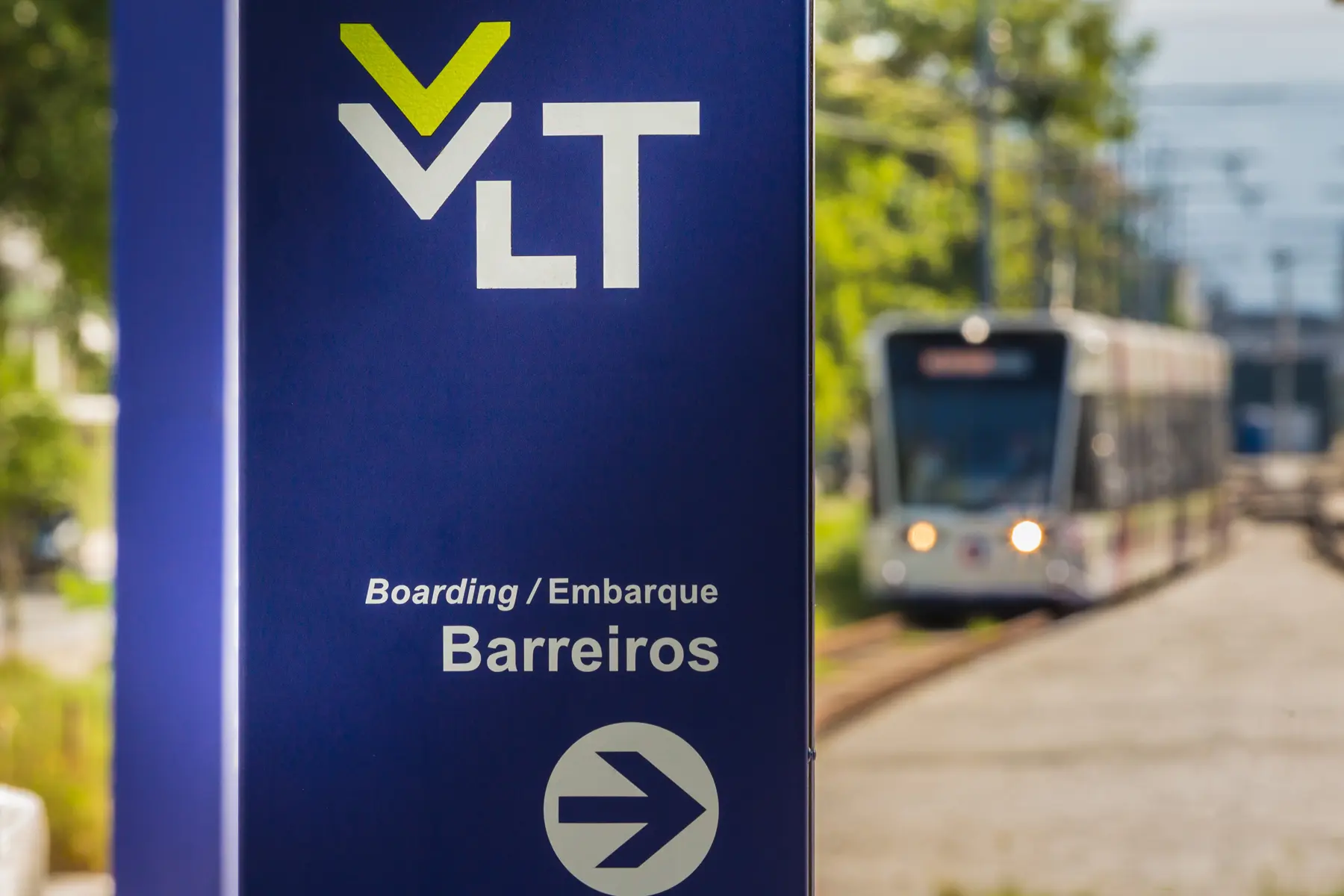 Placa da estação Barreiros do VLT com trem ao fundo em operação