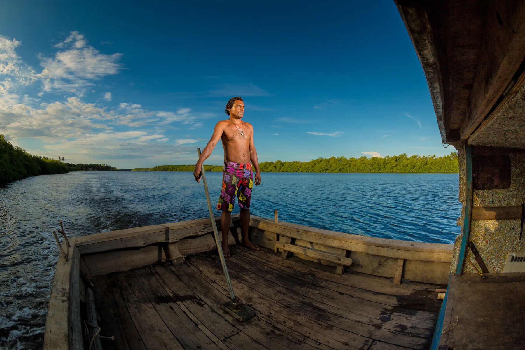 Trabalhador em embarcação tradicional navegando por área de vegetação nativa e manguezal no sul da Bahia