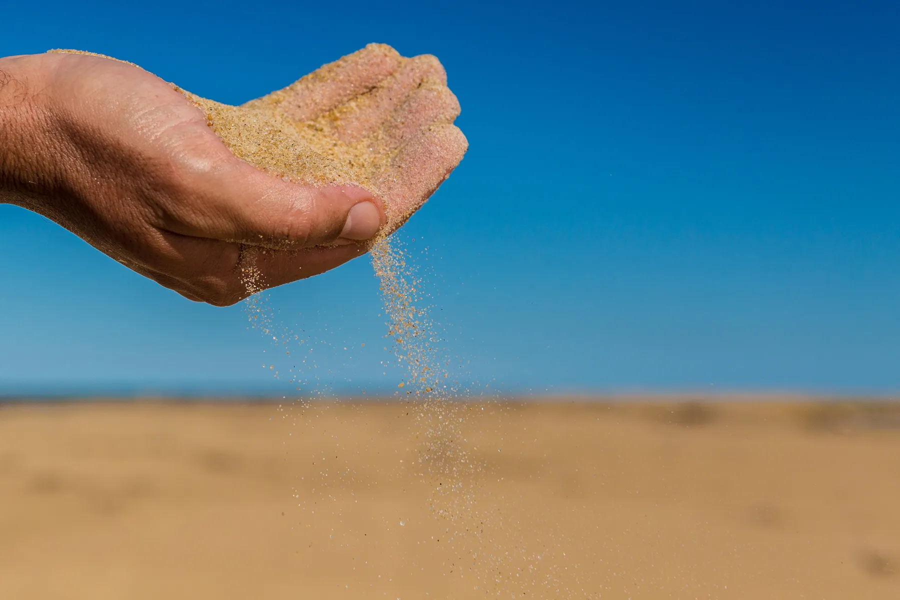 Mão deixando areia escorrer em ambiente árido, representando fragilidade ambiental e erosão costeira