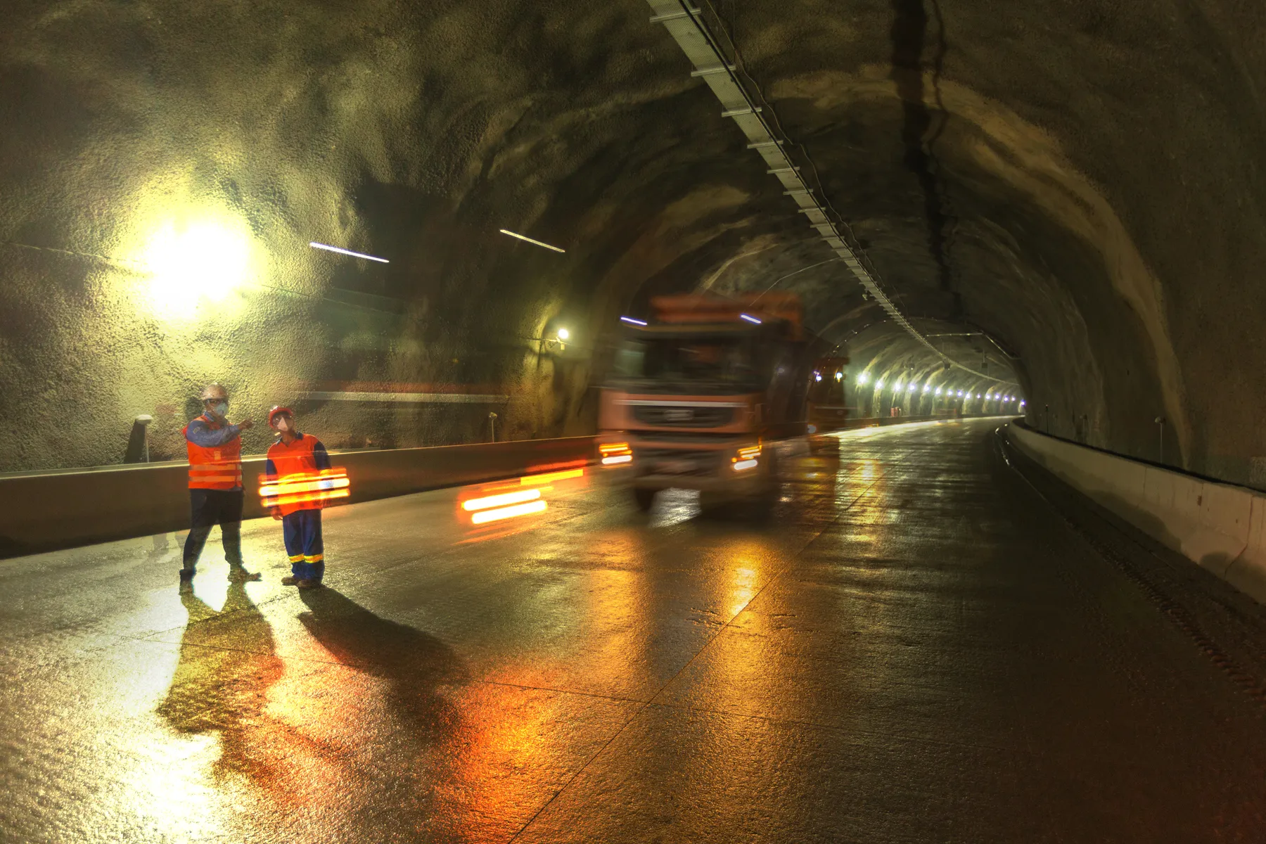 Interior de túnel dos Contornos da Tamoios com colaboradores e caminhão em movimento