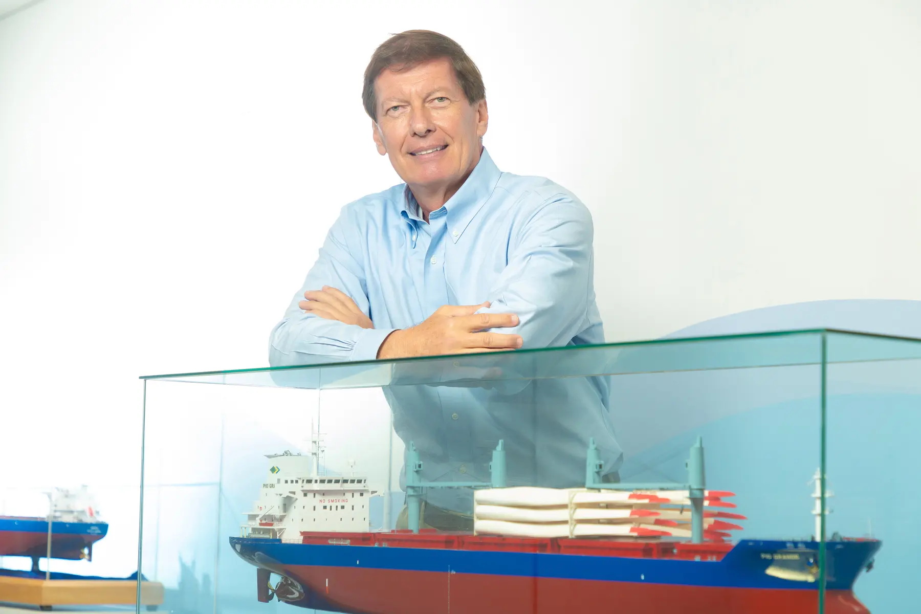 Homem sorridente com camisa azul clara atrás de vitrine com modelo de navio de carga da Norsul