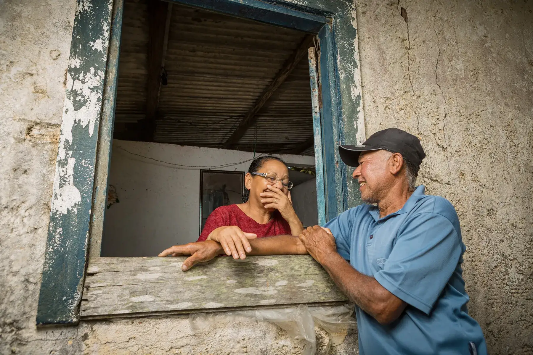 Moradores interagindo por janela em casa rústica em território costeiro do sul da Bahia