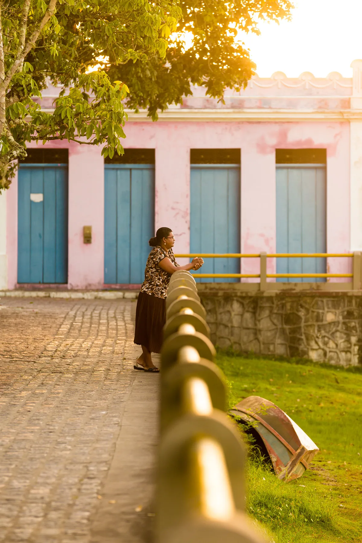 Mulher em Canavieiras (BA) diante de construções coloniais e barco costeiro virado na grama