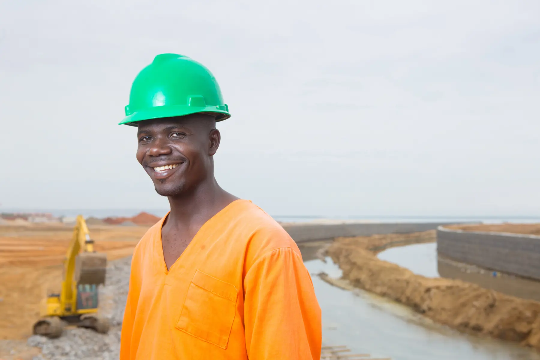 Trabalhador em obra de canalização na Praia de Luanda, Angola, com escavadeira ao fundo