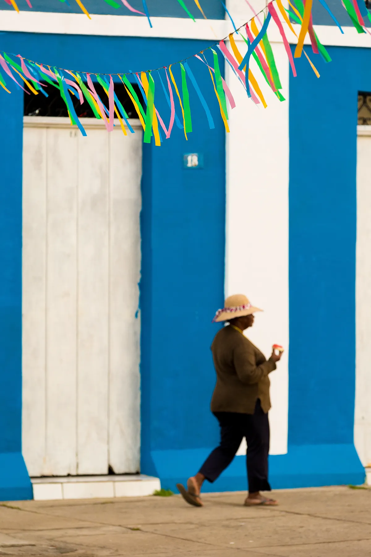 Pessoa com chapéu colorido diante de fachada azul decorada com bandeirolas em Canavieiras, sul da Bahia
