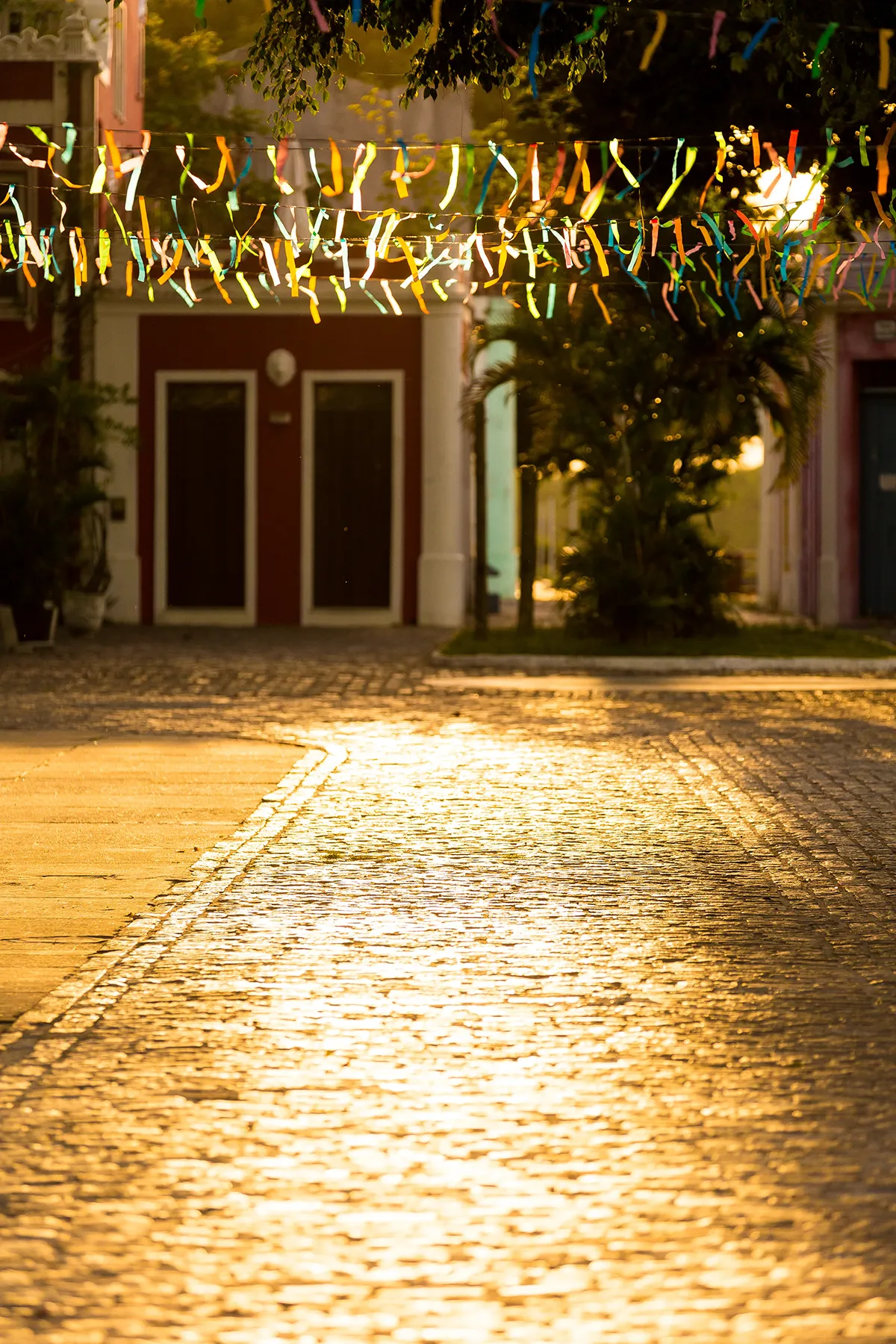 Rua de paralelepípedos com bandeirolas em Canavieiras, sul da Bahia, iluminada pelo sol dourado