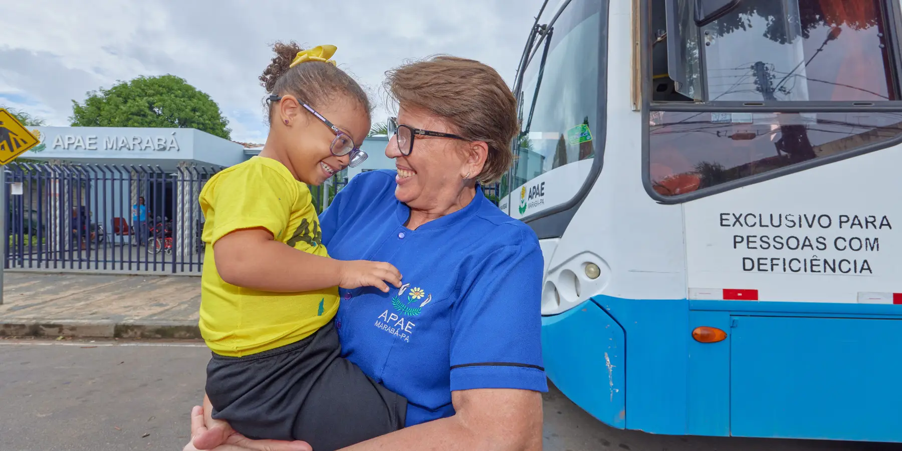 Pessoa com criança diante de ônibus adaptado da APAE em Marabá, Belém, promovendo inclusão e acolhimento