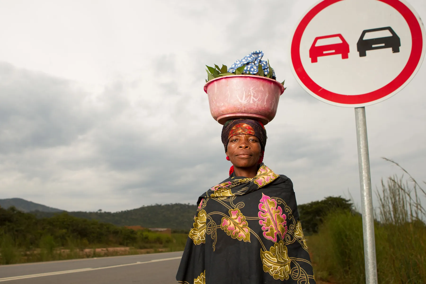 Pessoa típica de Angola com bacia na cabeça em estrada próxima ao Kwanza Sul, construída por empresa brasileira com respeito à cultura local