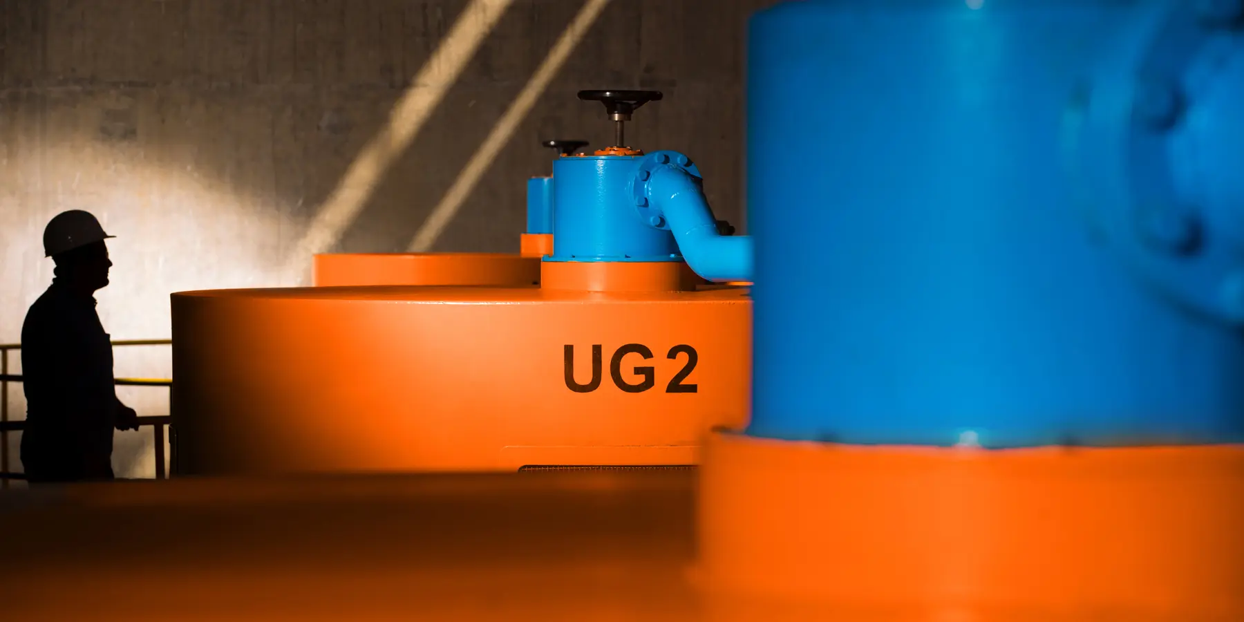 Interior de usina PCH com turbinas UG2 e colaborador em silhueta
