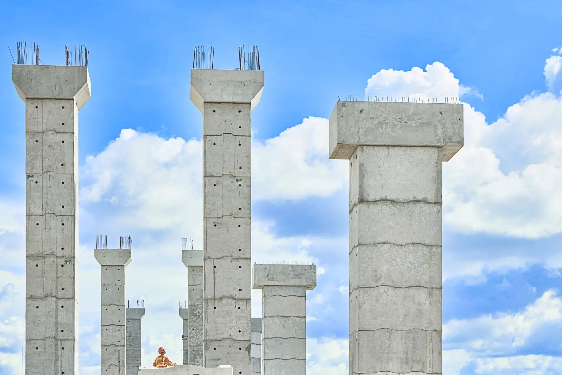 Pilares de ponte da Vale em construção, com trabalhador ao fundo e céu azul com nuvens