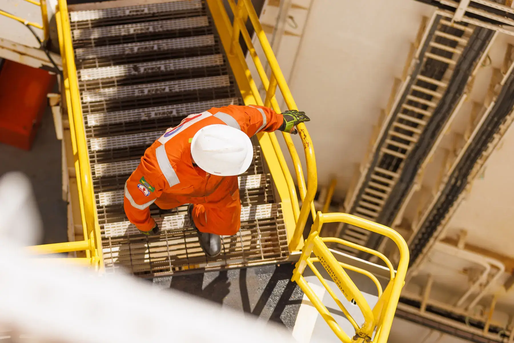 Colaborador em ambiente industrial sobe escada metálica com uso de EPI, evidenciando segurança operacional