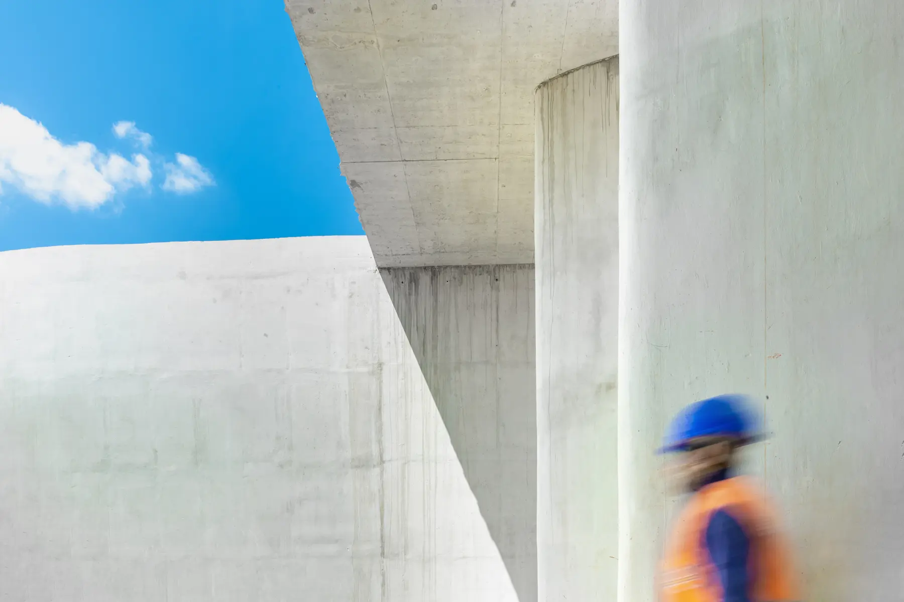 Colaborador com EPI diante de estrutura arquitetônica moderna em concreto, com céu azul ao fundo