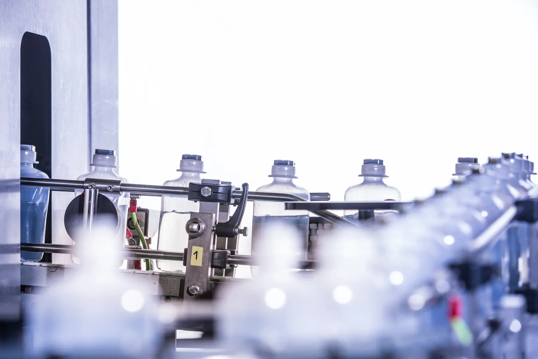 Frascos plásticos com tampas azuis em linha de envase automatizada em ambiente industrial.