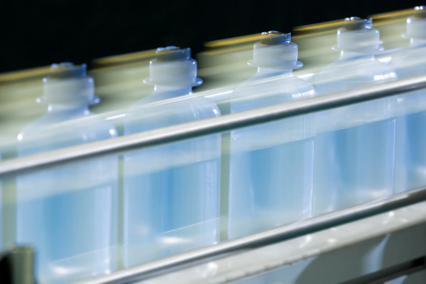 Frascos plásticos translúcidos em movimento sobre esteira automatizada em linha de produção industrial.