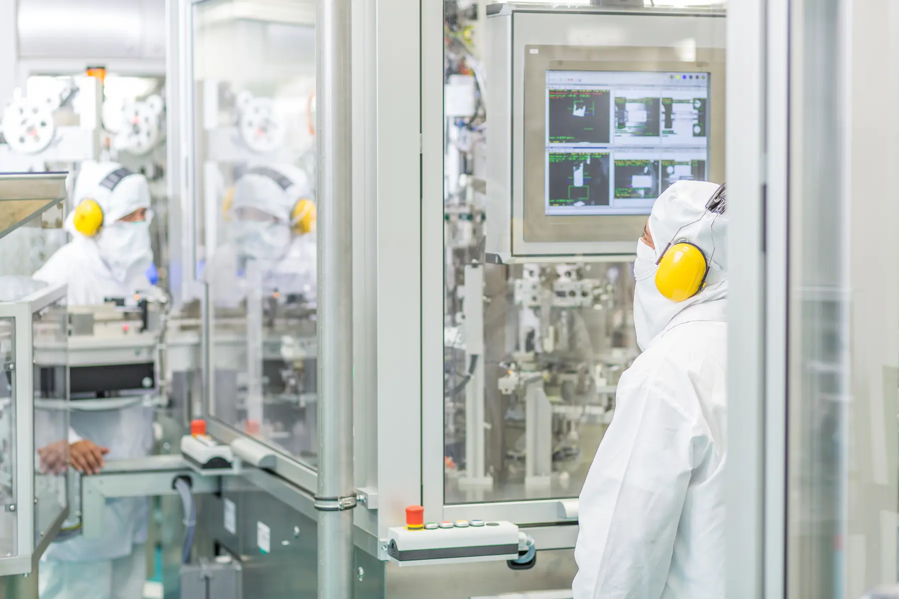 Profissionais em sala limpa monitorando interface de máquina em ambiente industrial estéril e automatizado.