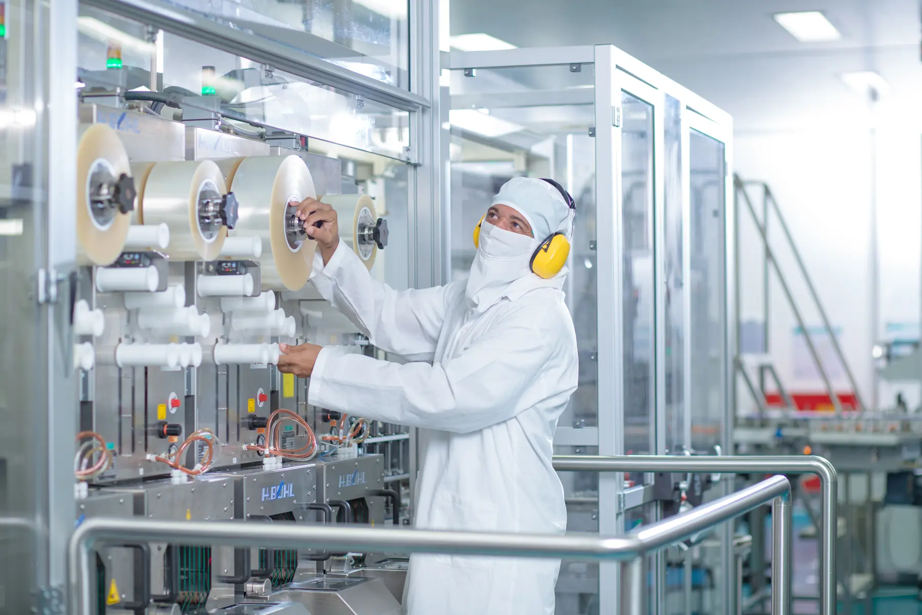 Profissional em sala limpa operando máquina com rolos em ambiente industrial estéril e controlado.