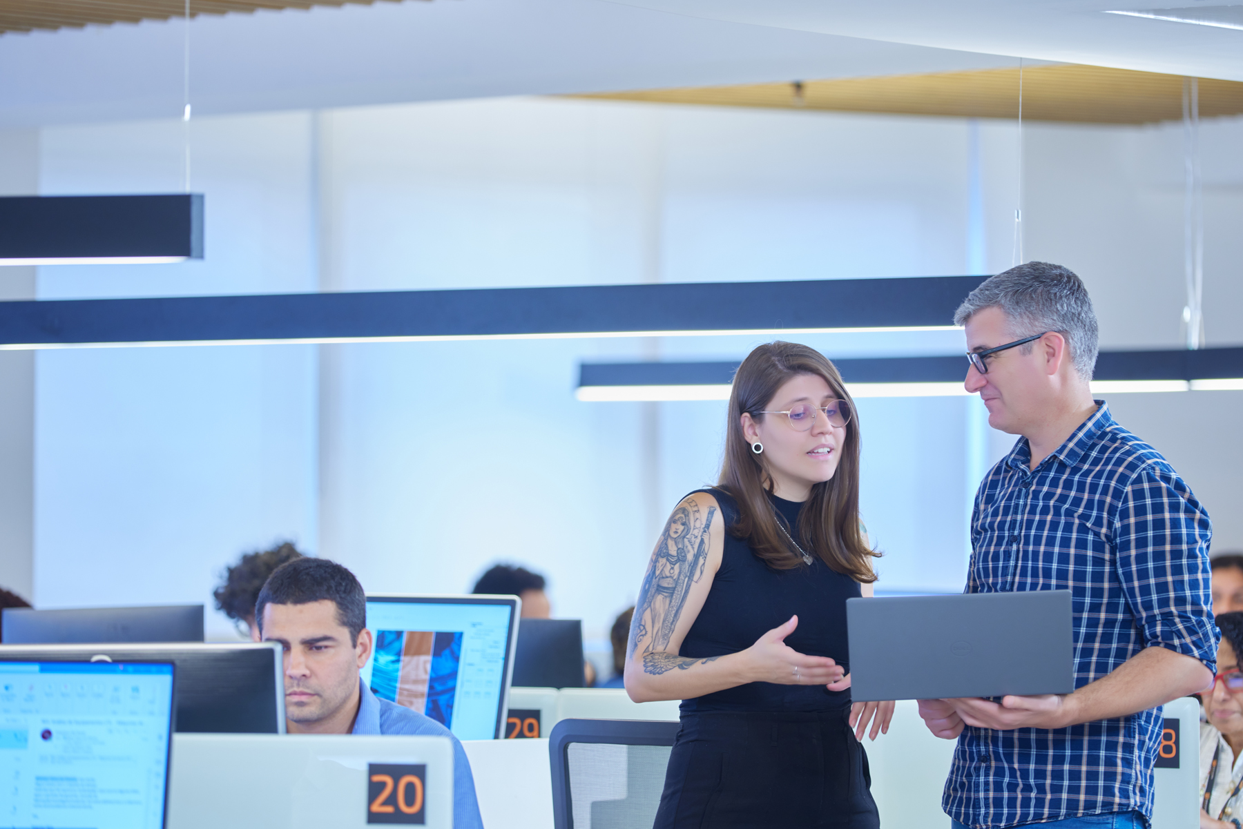 Duas pessoas conversando em escritório moderno com computadores e ambiente colaborativo