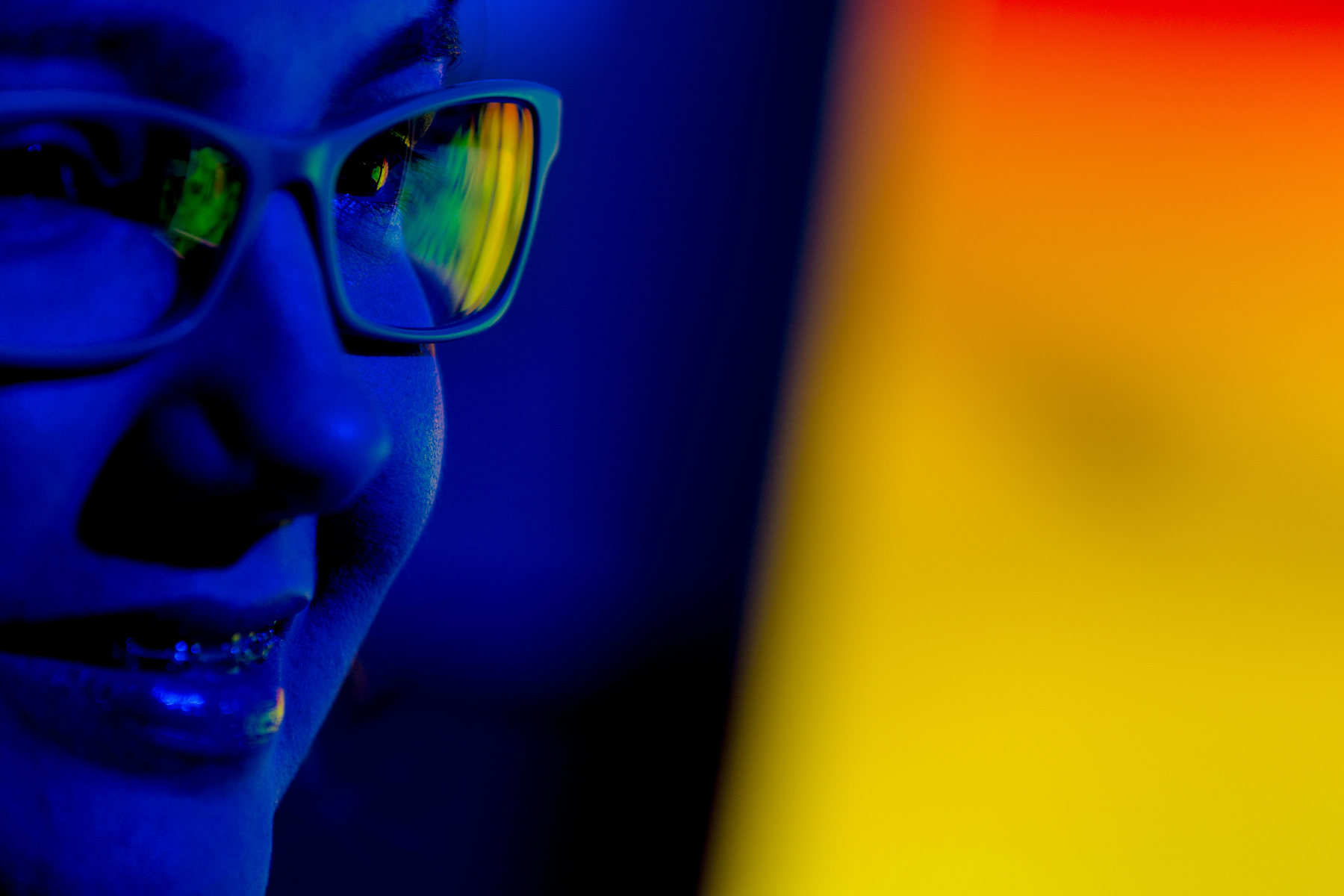 Rosto com óculos refletindo tela digital em ambiente com iluminação azul e amarela