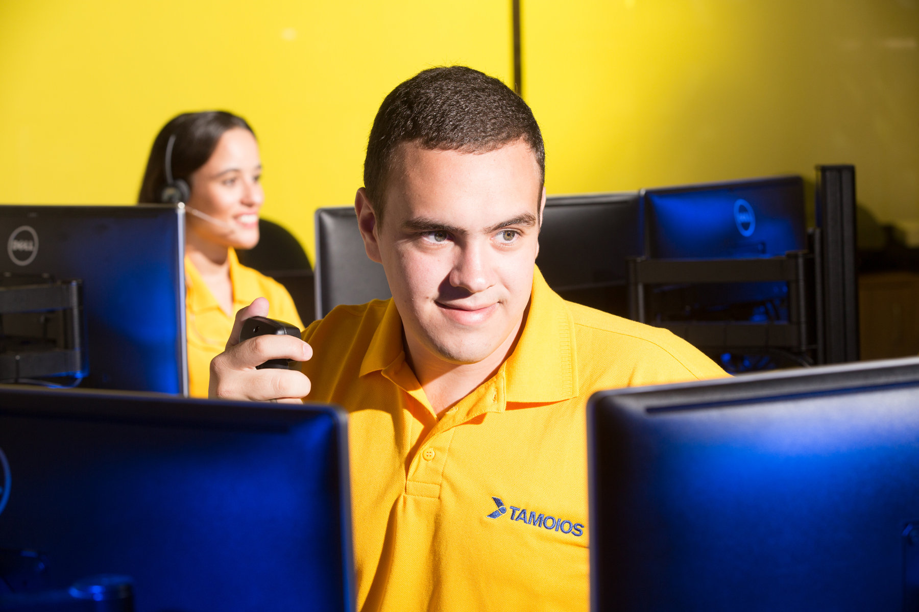 Pessoas com uniforme TAMOIOS em centro de operações com computadores e equipamentos de comunicação