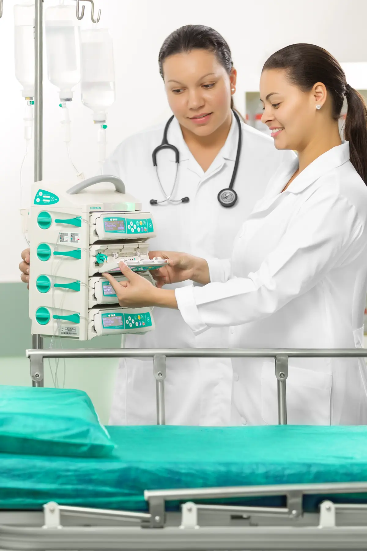 Profissionais da saúde operando bomba de infusão múltipla B. Braun ao lado de leito hospitalar.