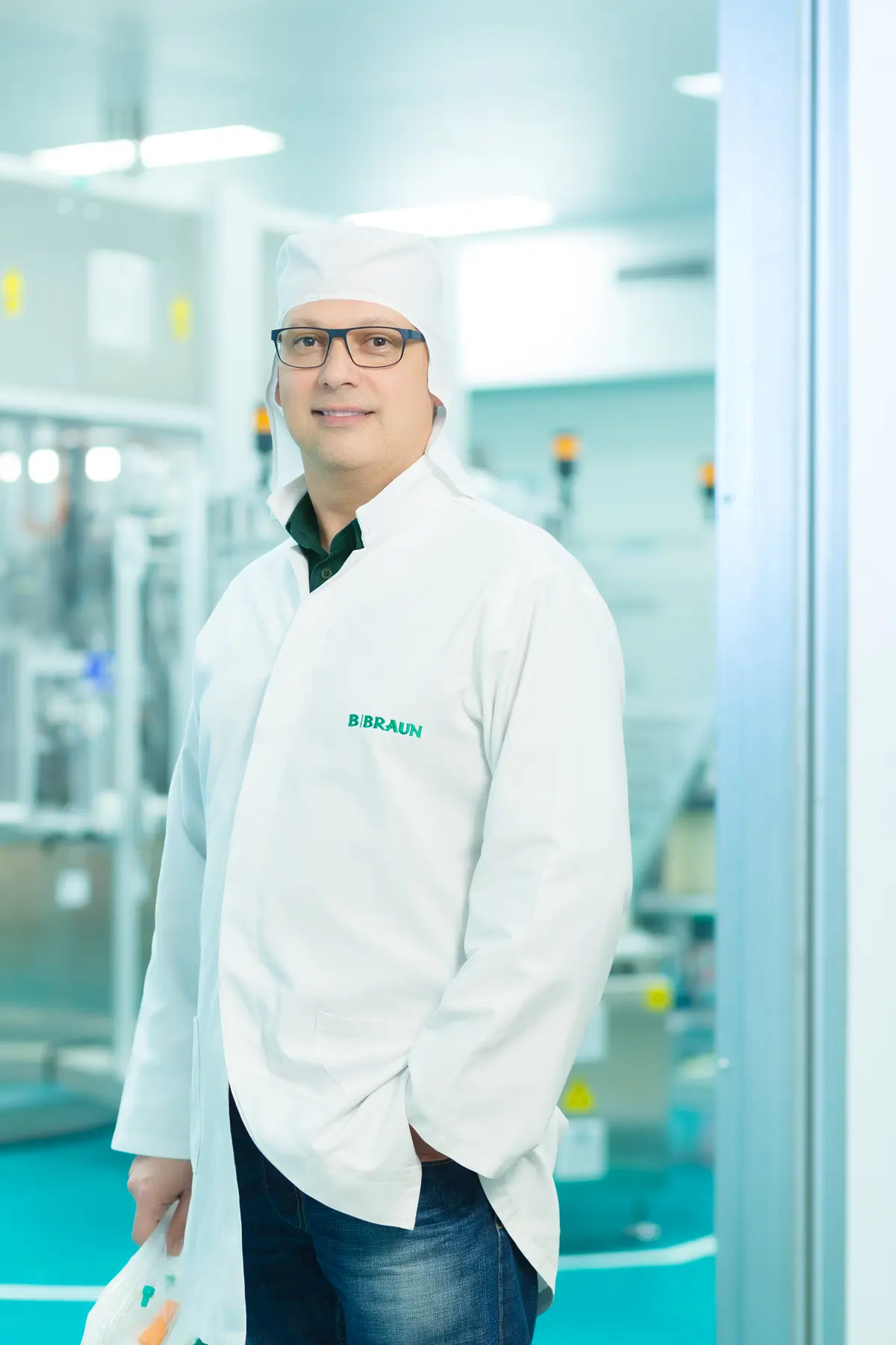 Colaborador da B. Braun em sala limpa com jaleco branco e item médico em ambiente industrial controlado.