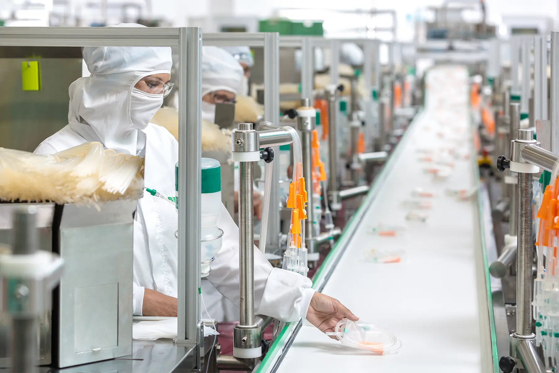 Funcionários em sala limpa operando linha de produção automatizada de seringas e tubos médicos descartáveis.