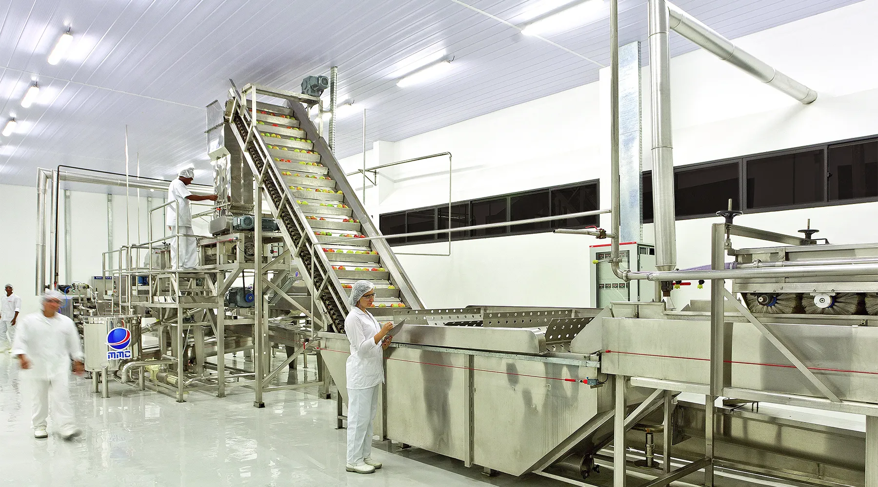 Funcionários operando linha de processamento de alimentos com frutas em ambiente industrial higienizado.