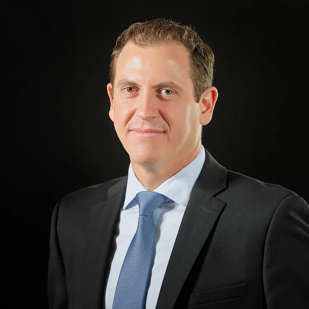 Retrato profissional de Daniel Rachman, CFO da Constellation, em traje formal sobre fundo preto.