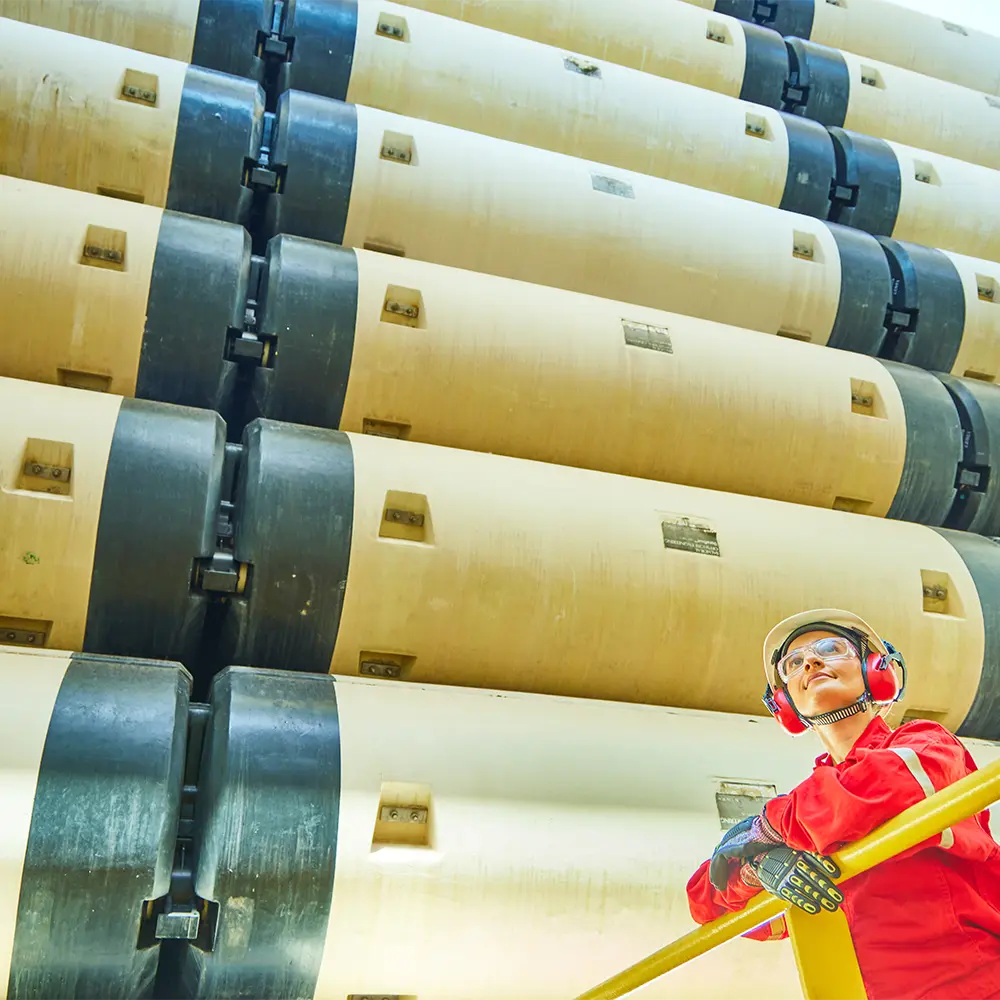 Trabalhador com EPI observando risers empilhados em navio sonda, em ambiente industrial offshore.