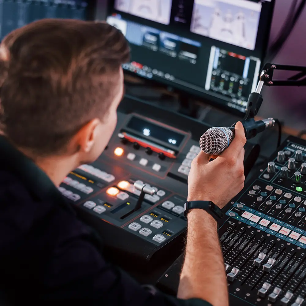Técnico operando mesa de som e vídeo em estúdio, ajustando controles e monitorando transmissões