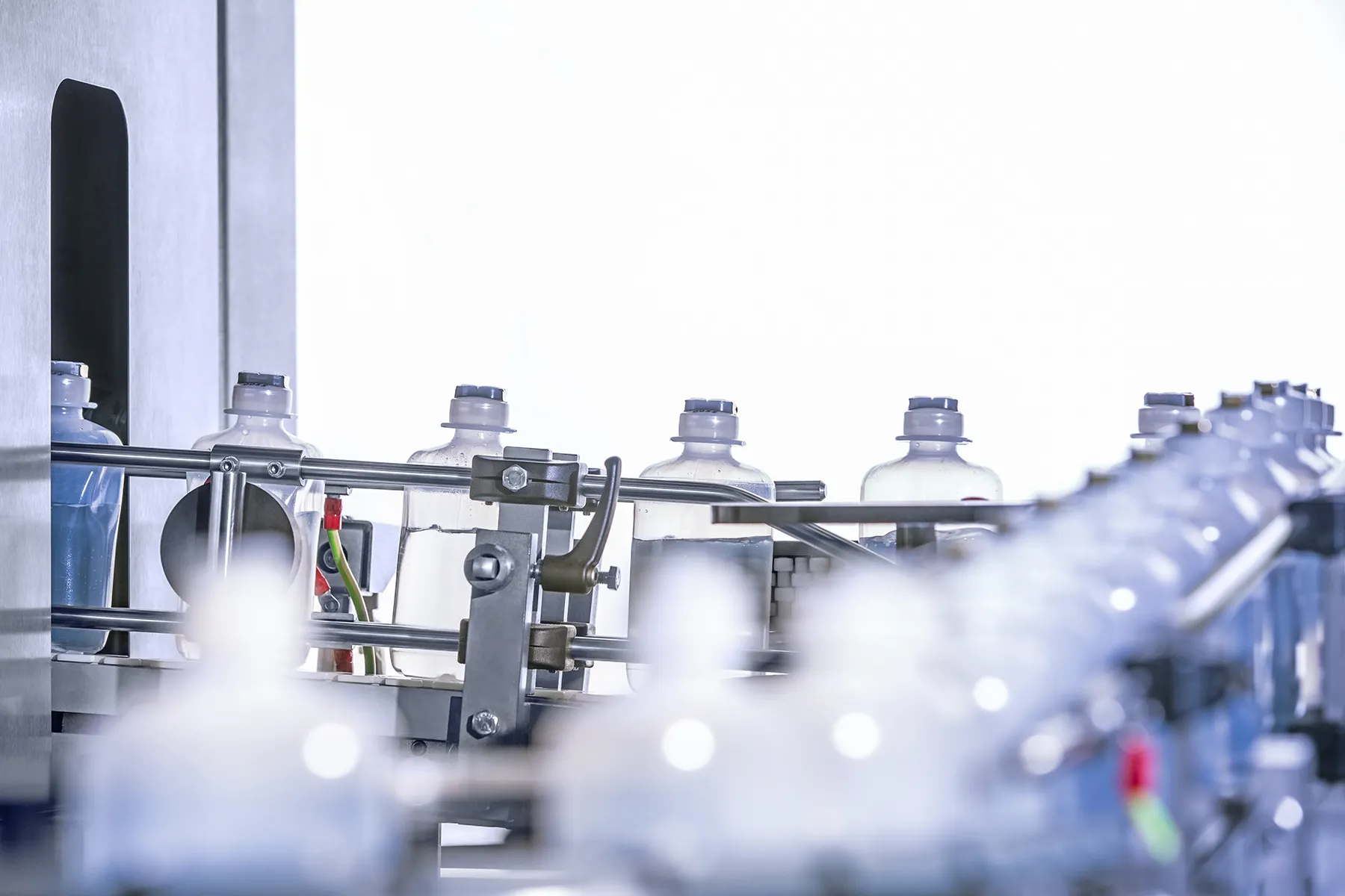 Frascos plásticos com tampas azuis em linha de envase automatizada em ambiente industrial.