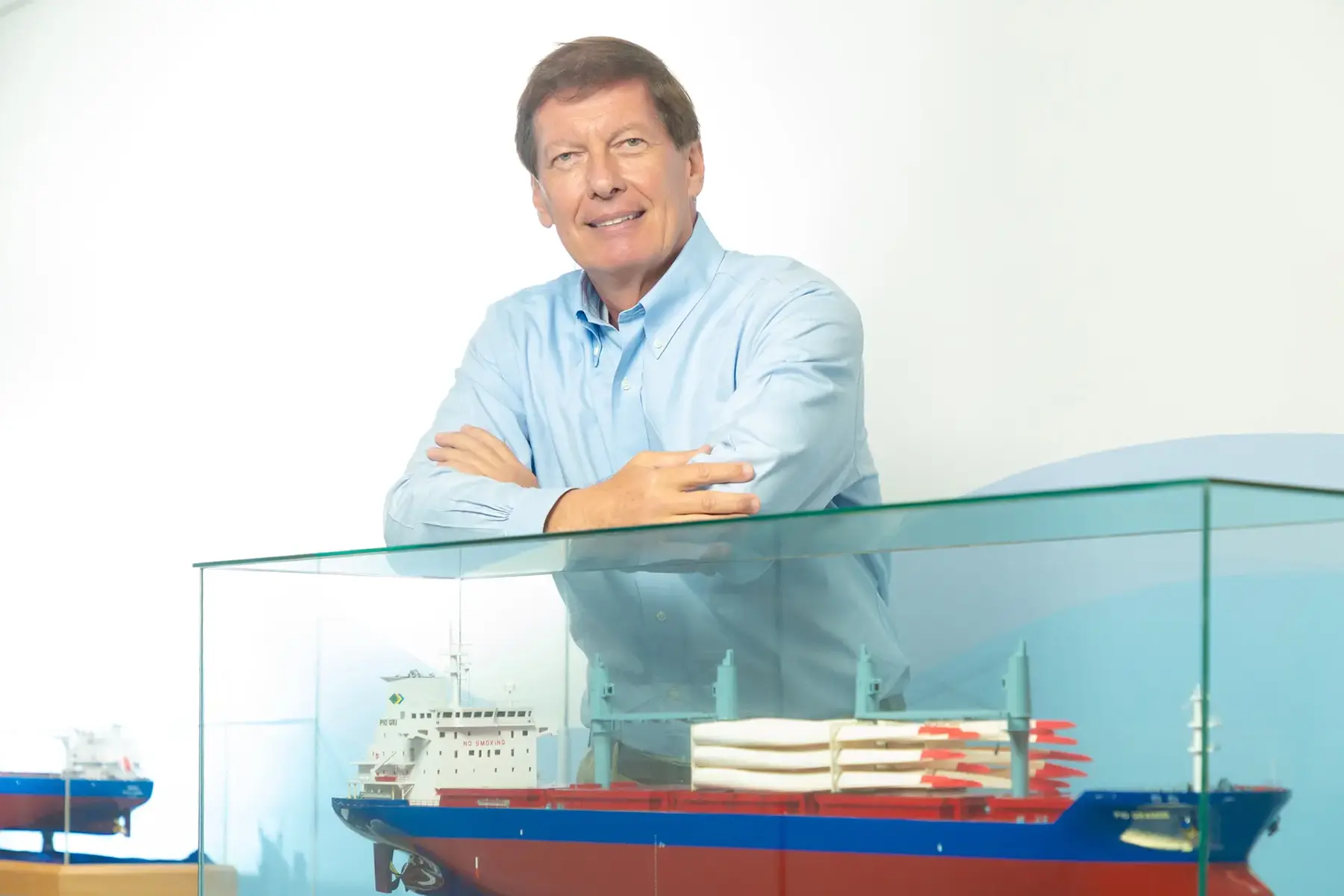 Homem sorridente com camisa azul clara atrás de vitrine com modelo de navio de carga da Norsul